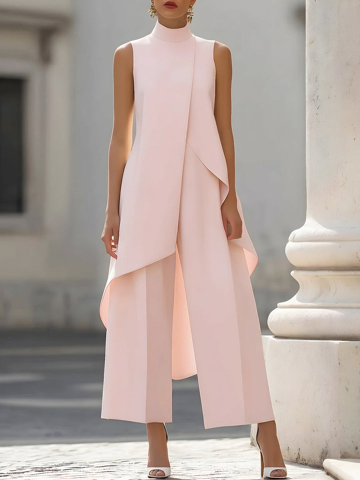 Lichtroze set met asymmetrische top en wijde broek, gedragen door een model voor een witte zuil. 7