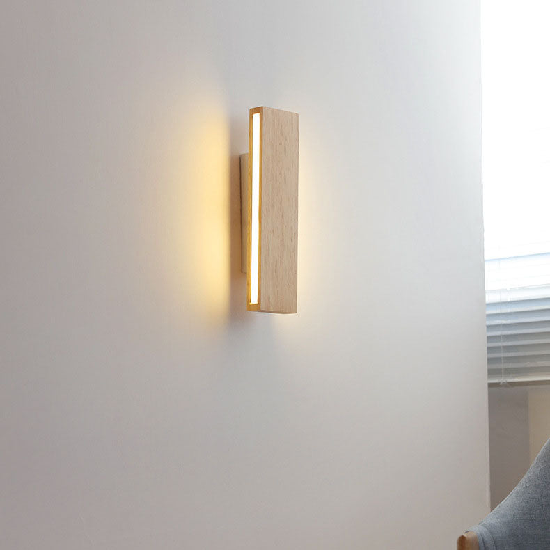 Brandende verticale houten wandlamp aan een lichte muur, met warm licht en een raam met jaloezie en stoel ernaast. 15