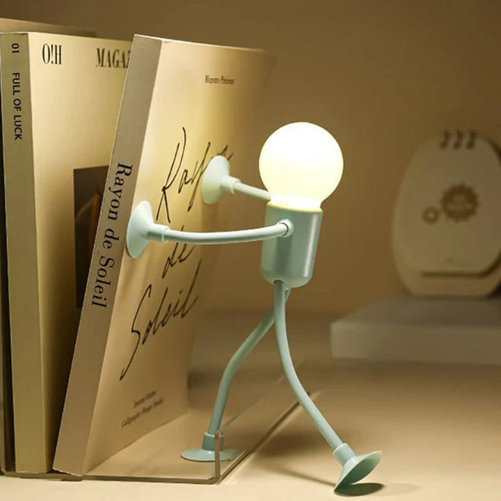 Groen mannetjeslampje dat met zijn zuignappen tegen een boekenrug duwt, op een plank met boeken en een zacht gloeiende lamp. 9