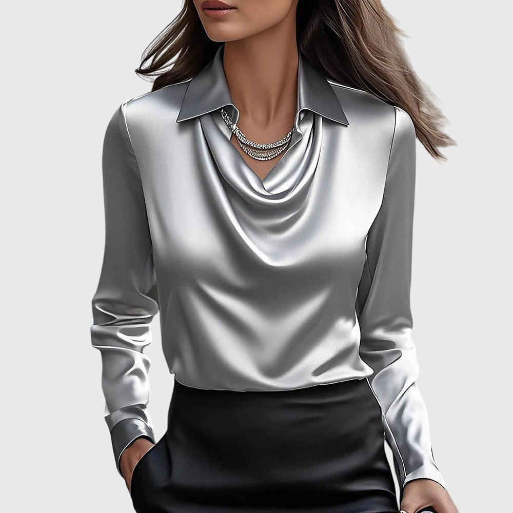Model draagt de zilvergrijze satijnblouse met gedrapeerde halslijn, kraag en lange mouwen, met een zwarte rok en strassketting. 2