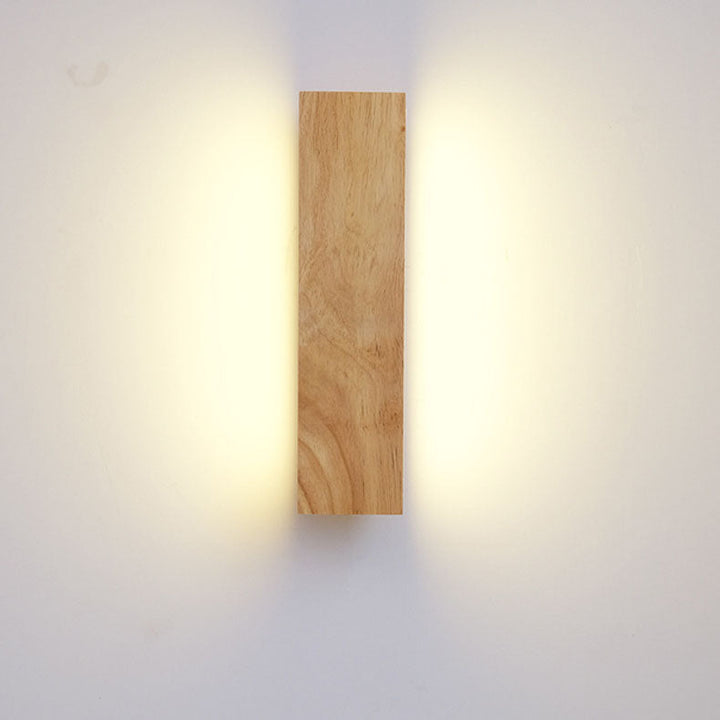 Verticale houten wandlamp van voren gezien, brandend, met warm licht dat links en rechts langs de muur schijnt. 3