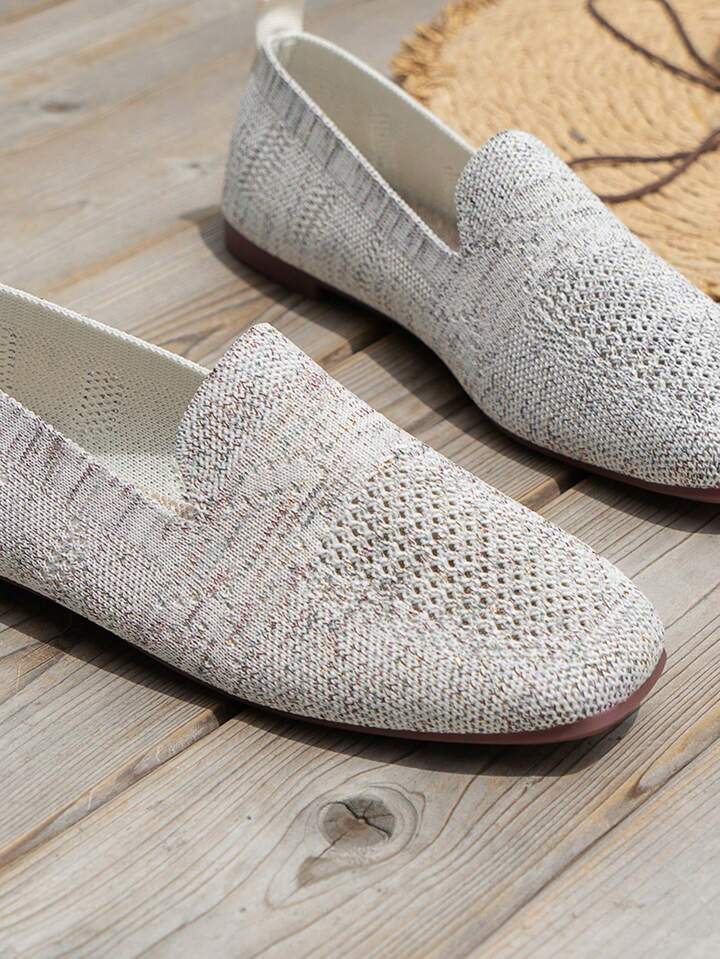 Close-up van lichtgrijze gebreide instapschoenen met open mesh op de neus en ronde voorkant, liggend op een houten vloer. 16