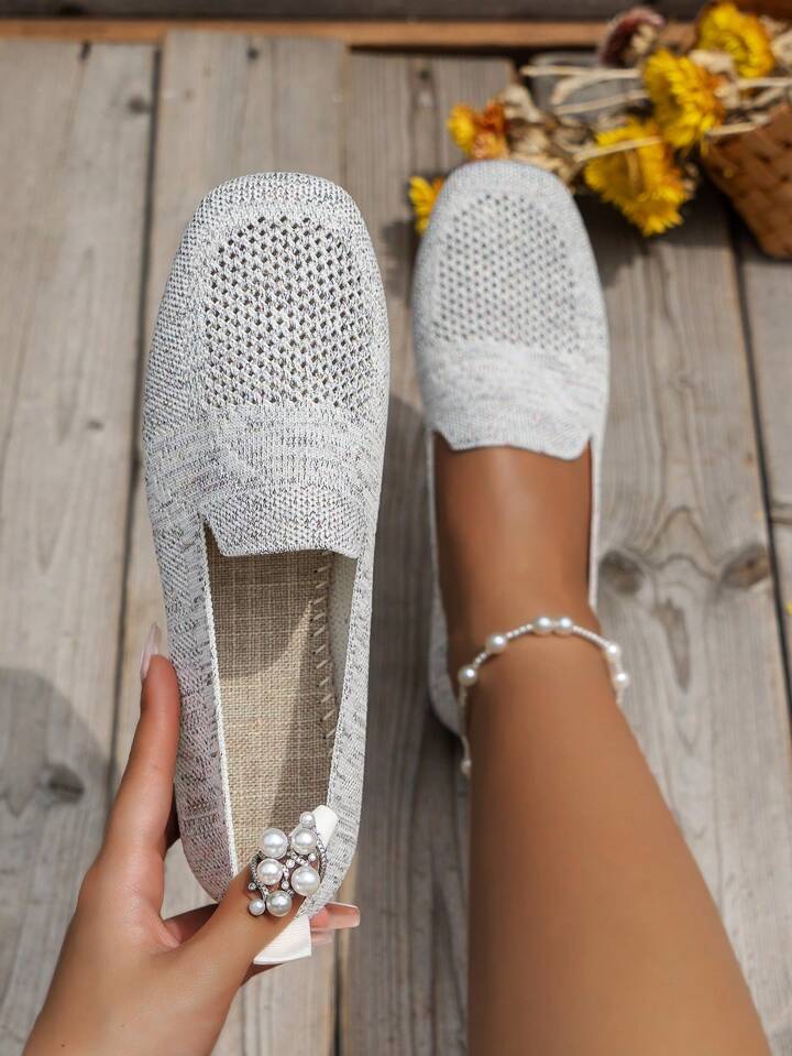 Lichtgrijze mesh instapschoenen van bovenaf; een schoen wordt vastgehouden en toont het stoffen voetbed, met gele bloemen op de achtergrond. 15