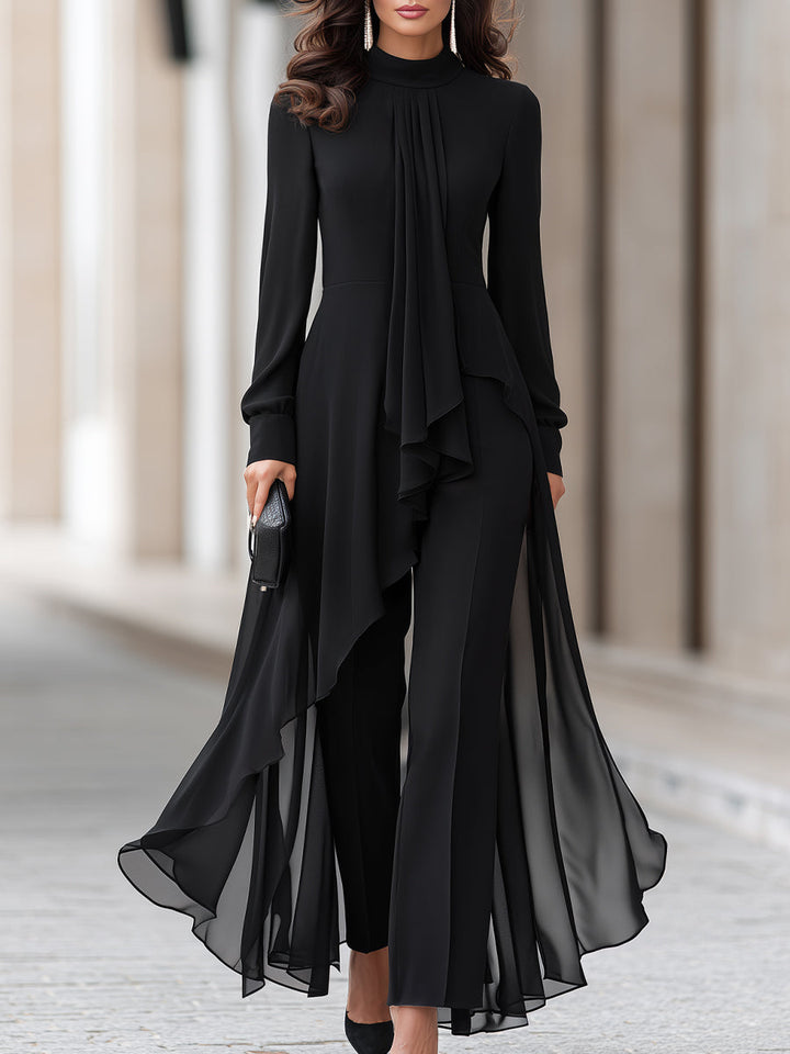 Vrouw in zwarte chiffon tuniek met wijde broek op straat, bijgesneden vanaf de kin tot de voeten, met clutch in de hand. 1