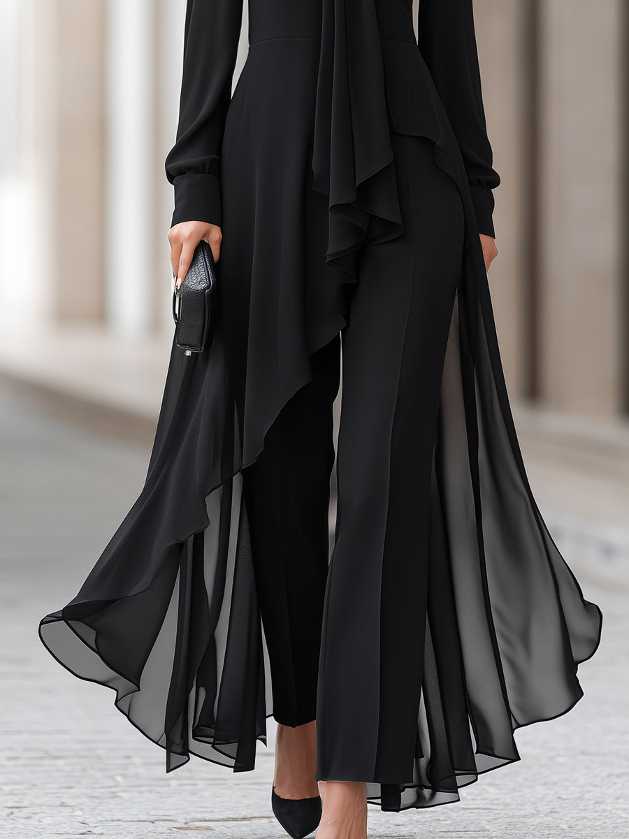 Detail van het onderste deel: asymmetrisch vallende doorschijnende chiffon tuniek over zwarte broek met wijde pijpen, model draagt zwarte pumps. 4