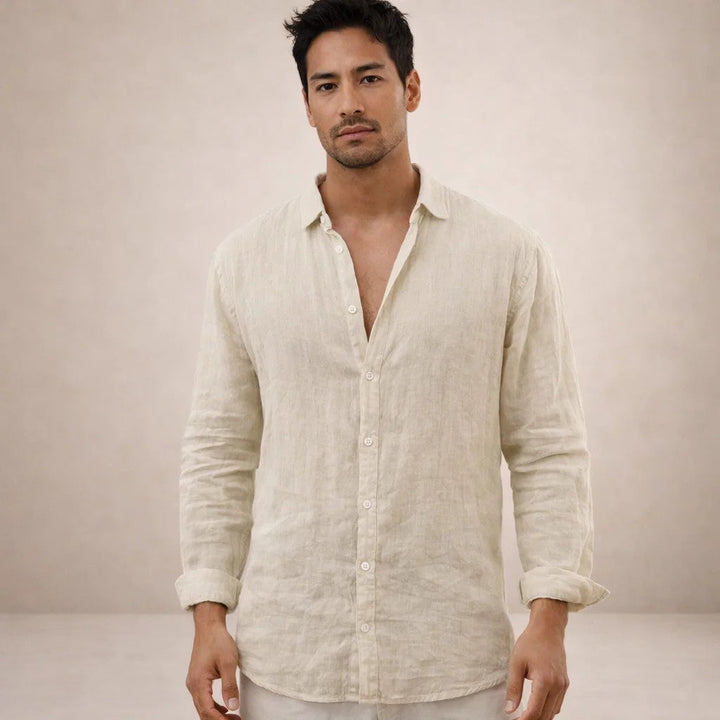 Model kijkt in de camera en draagt een beige linnen overhemd met kraag, opgerolde mouwen en een lichte broek. 11