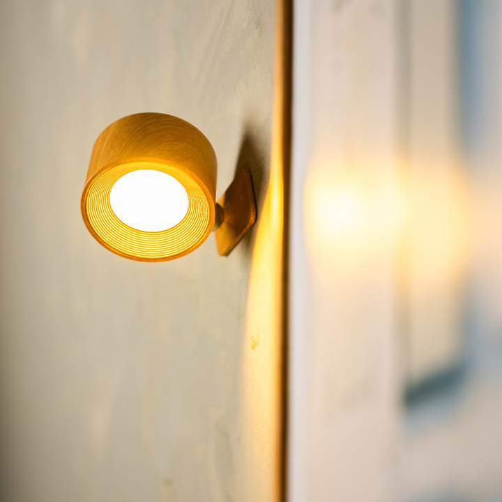 Close-up van de houtkleurige wandlamp met brandende lichtschijf en fijne ribbels in de binnenrand. 15