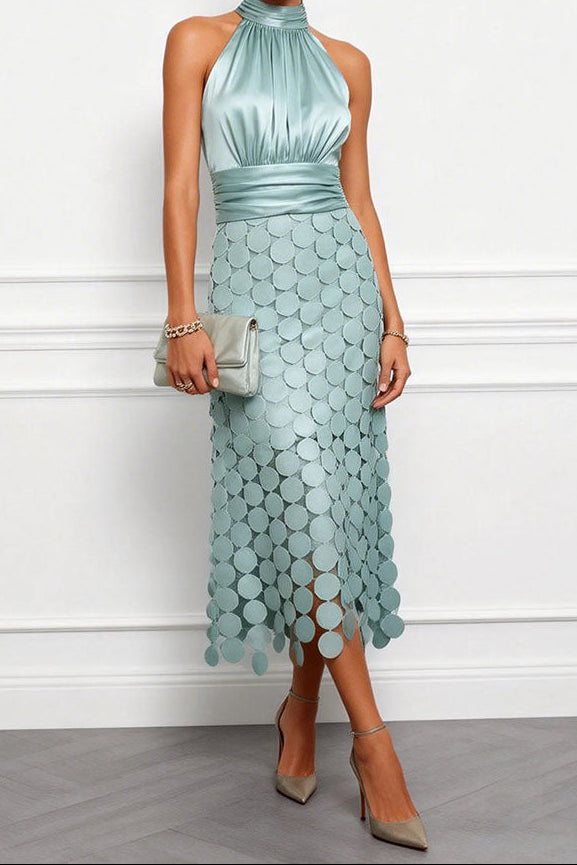 Dezelfde halterjurk in zacht mintgroen, gedragen door een model met lichte clutch en taupekleurige pumps voor een witte wand. 2