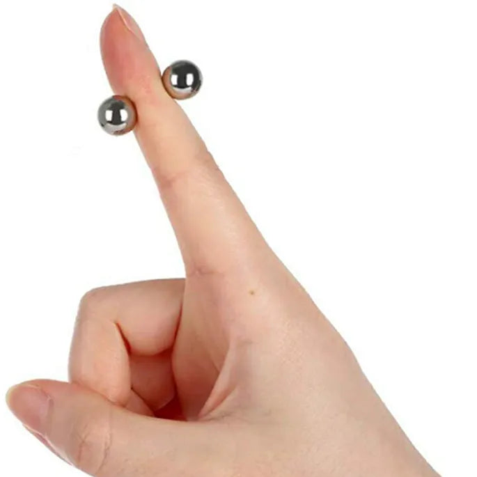 Opgestoken vinger met twee kleine zilverkleurige magneetbolletjes aan weerszijden van de vingertop, voor het formaat en de magnetische hechting. 8