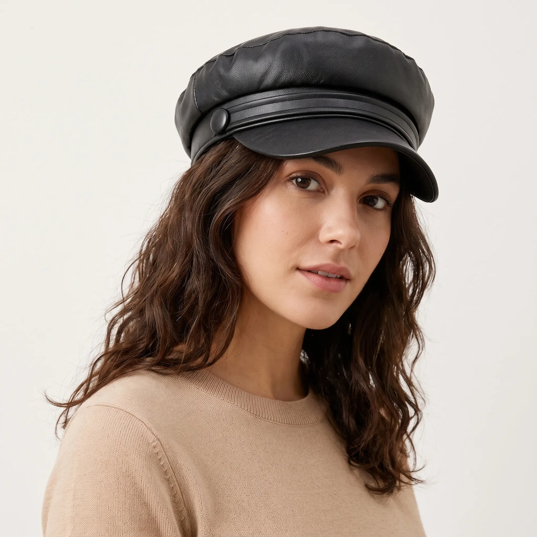 Vrouw met golvend bruin haar draagt de zwarte lederlook bakkerspet met knoop, schuin van opzij gefotografeerd 1