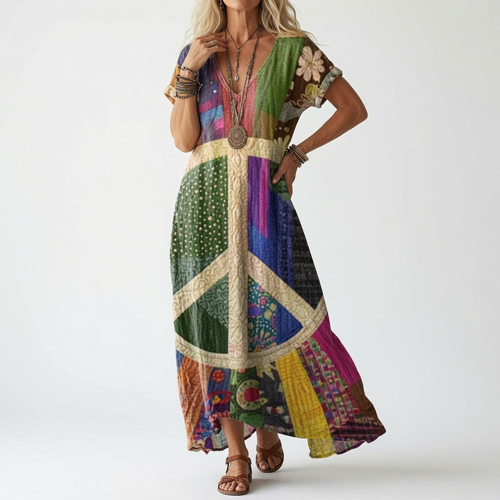 Model draagt de jurk in een kleurrijke patchworkversie met een groot vredesteken in het midden, met armbanden en bruine sandalen. 2