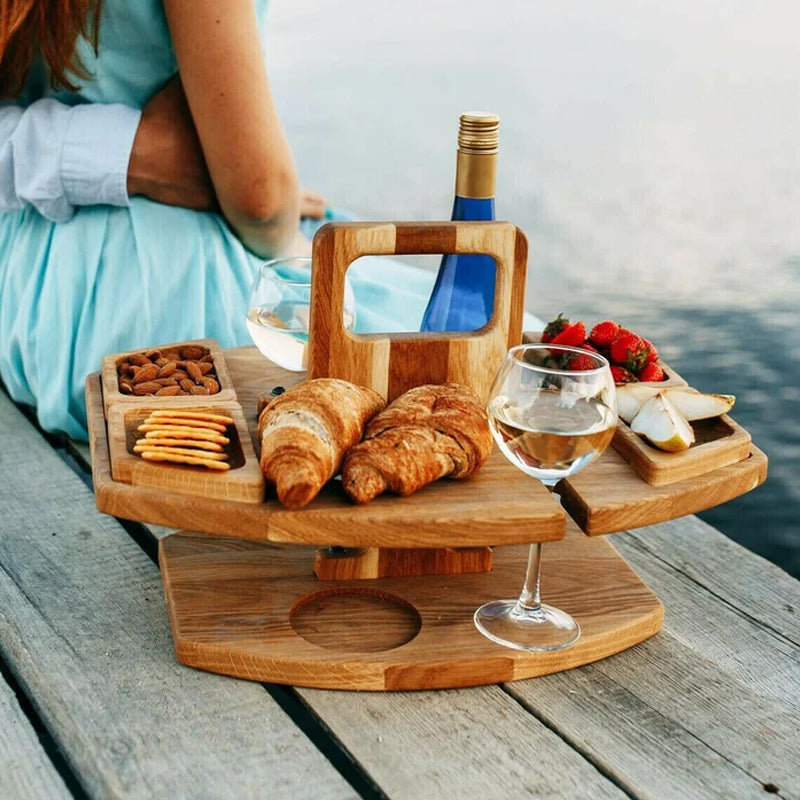 Wijntafel op een steiger aan het water met croissants, amandelen, crackers, fruit en een zittende vrouw 3