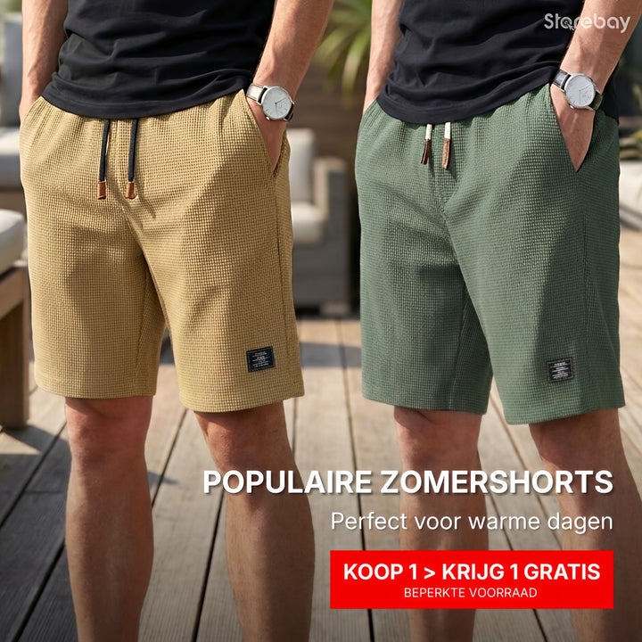 Twee mannen naast elkaar in korte wafelstructuur shorts, de ene zandkleurig en de andere groen, met handen in de zakken op een terras. 1