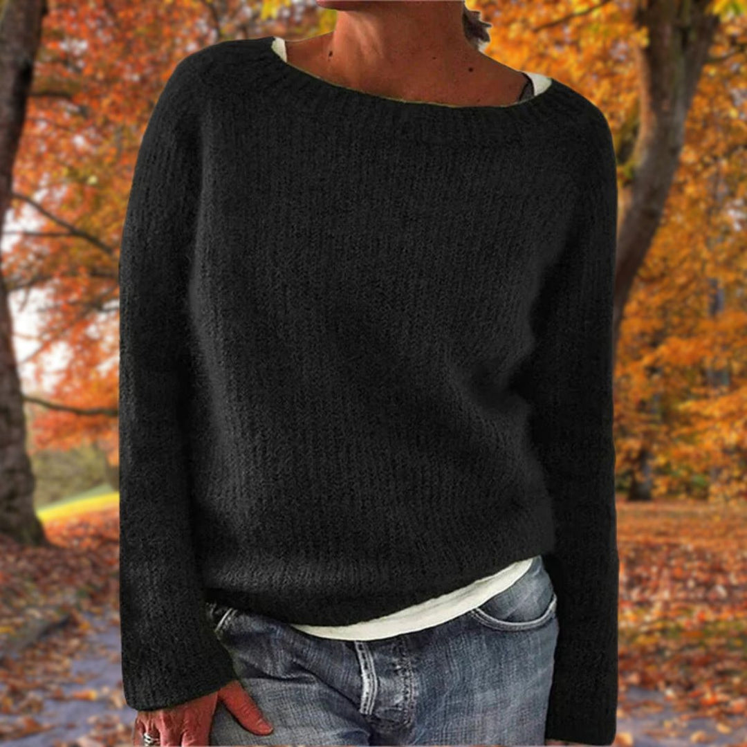 Vrouw draagt de gebreide trui in zwart over een wit shirt en spijkerbroek, in een herfstachtig bos. 2