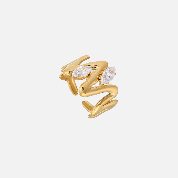 Goudkleurige open ring met golvend, vloeiend gevormd ontwerp en twee heldere marquise-stenen, schuin van boven gefotografeerd op een lichte achtergrond. 1