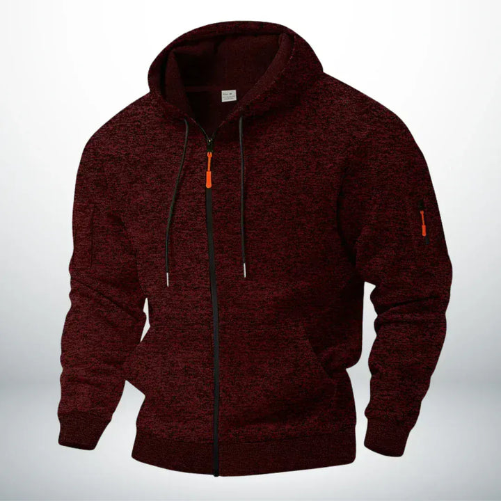 Dezelfde hoodie in gemêleerd donkerrood, schuin van voren gefotografeerd met zichtbare ritszak op de mouw en oranje trekker. 2