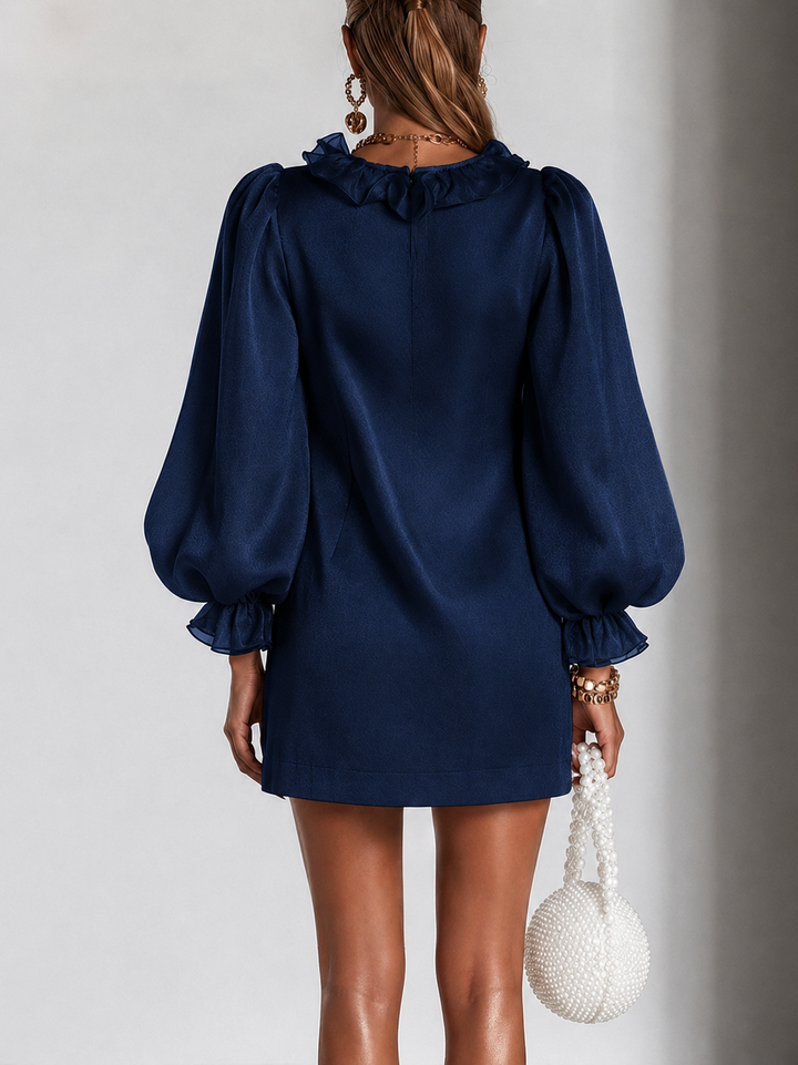 Achterkant van de marineblauwe jurk met ruchekraag, ritssluiting in de rug, pofmouwen en ruchemanchetten, gedragen door een model. 7