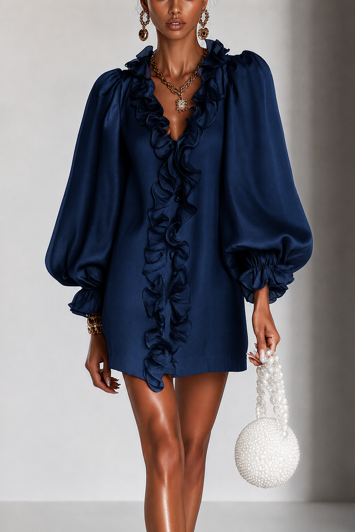 Model draagt de jurk in marineblauw met ruches langs de V-hals en pofmouwen, met gouden sieraden en parelhandtas. 2
