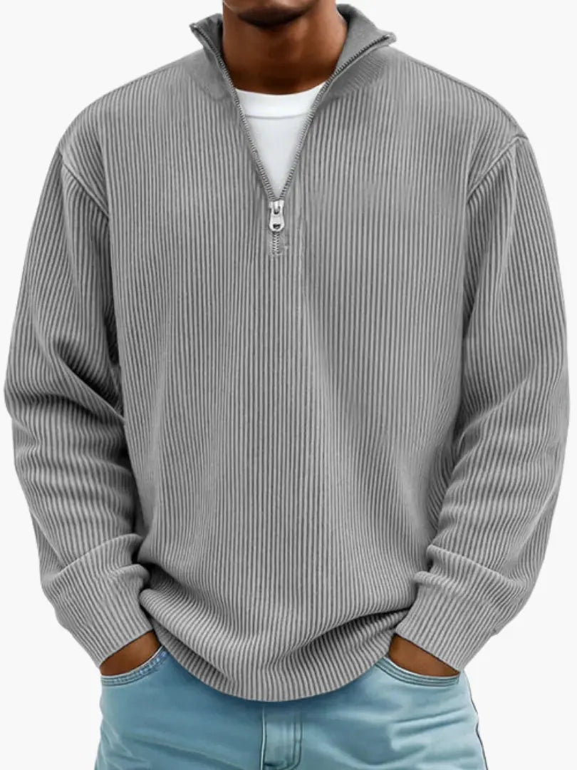 Model draagt de geribbelde trui met kwartrits in grijs, een wit shirt eronder en handen in de broekzakken. 2