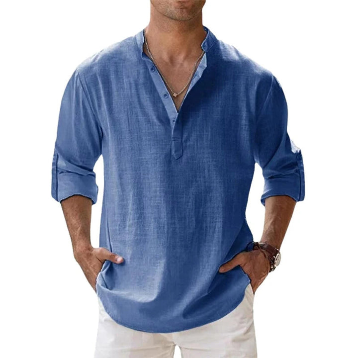Man draagt het Henley overhemd in blauw met opgerolde mouwen en knoopsluiting, gecombineerd met een witte broek. 2