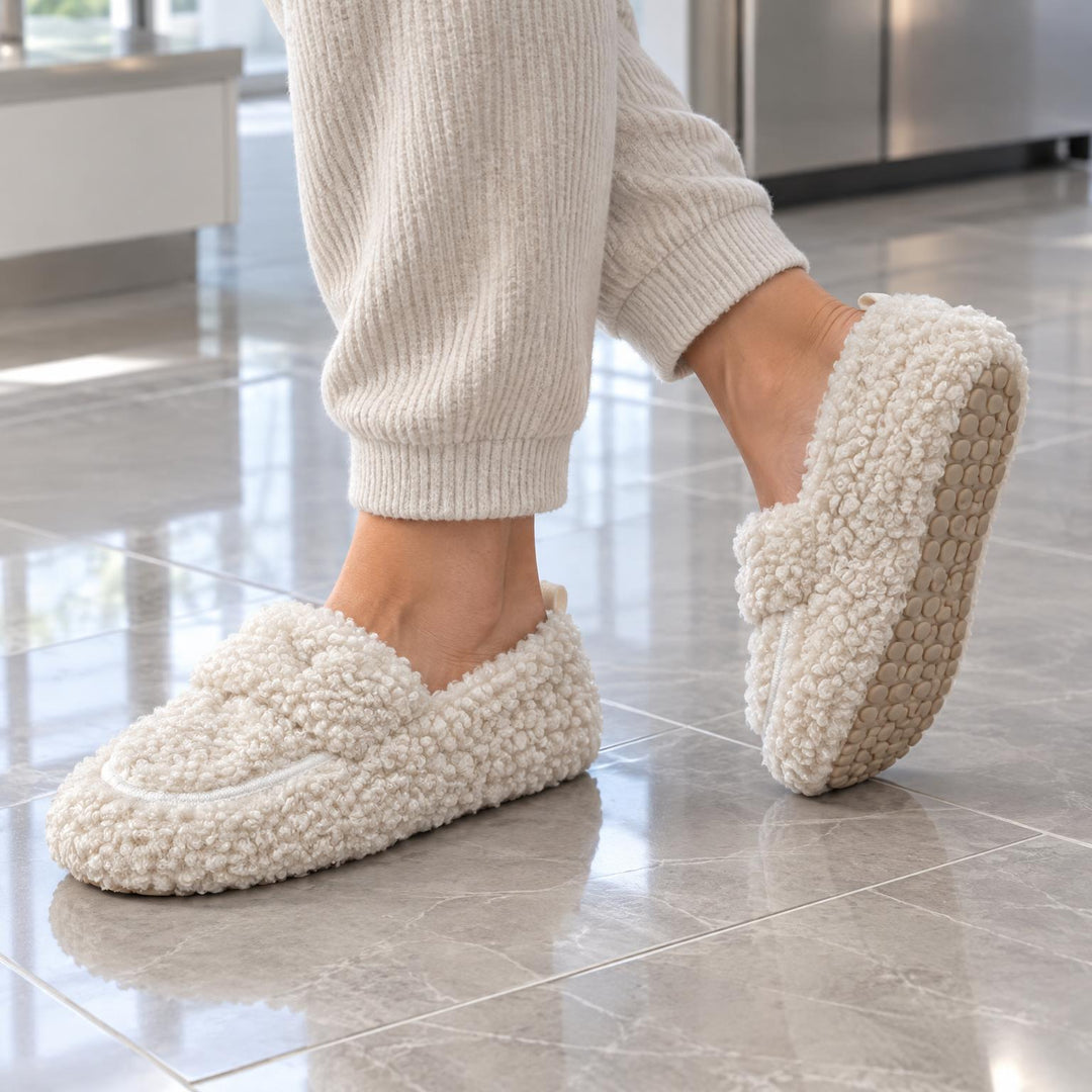Model loopt op een glanzende tegelvloer met crèmekleurige pluizige instappers en toont de noppenzool 1