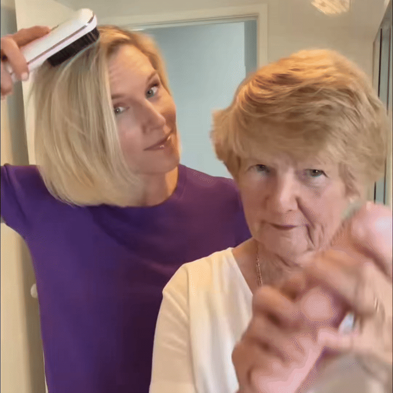 Blonde vrouw in paars shirt stylt haar haar met een witte borstel, naast een oudere vrouw met kort haar. 9