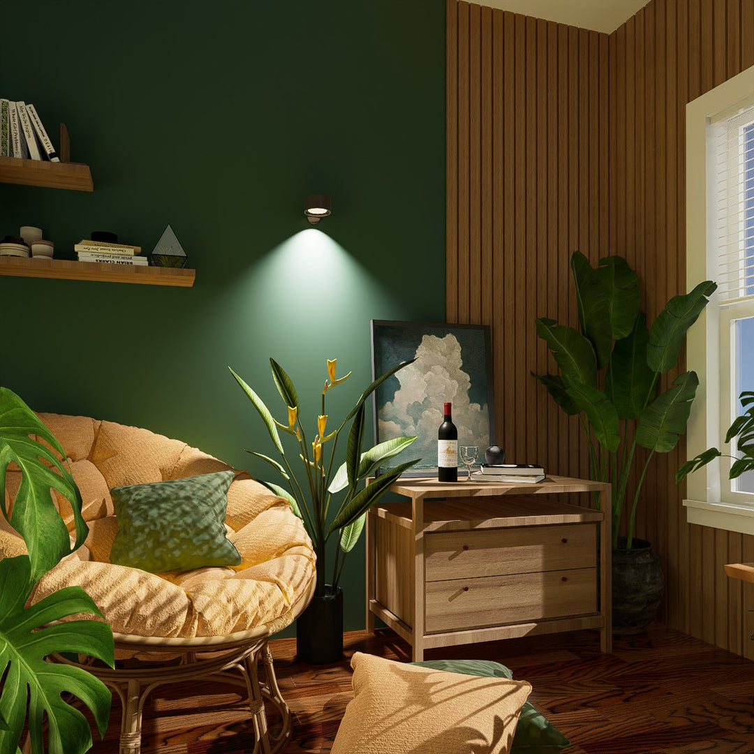 Wandlamp op een donkergroene muur werpt een lichtkegel in een hoek met rotanstoel, planten en houten lambrisering. 9