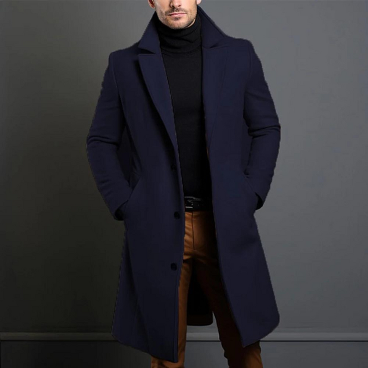 Model draagt de lange overjas in donkerblauw met een zwarte coltrui en bruine broek, de overjas dicht met drie knopen. 4