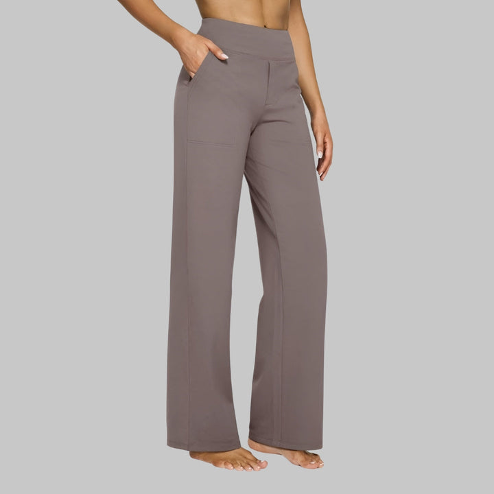 Model in taupe broek met hoge taille en rechte pijp, zijaanzicht, met een hand in de zijzak. 1