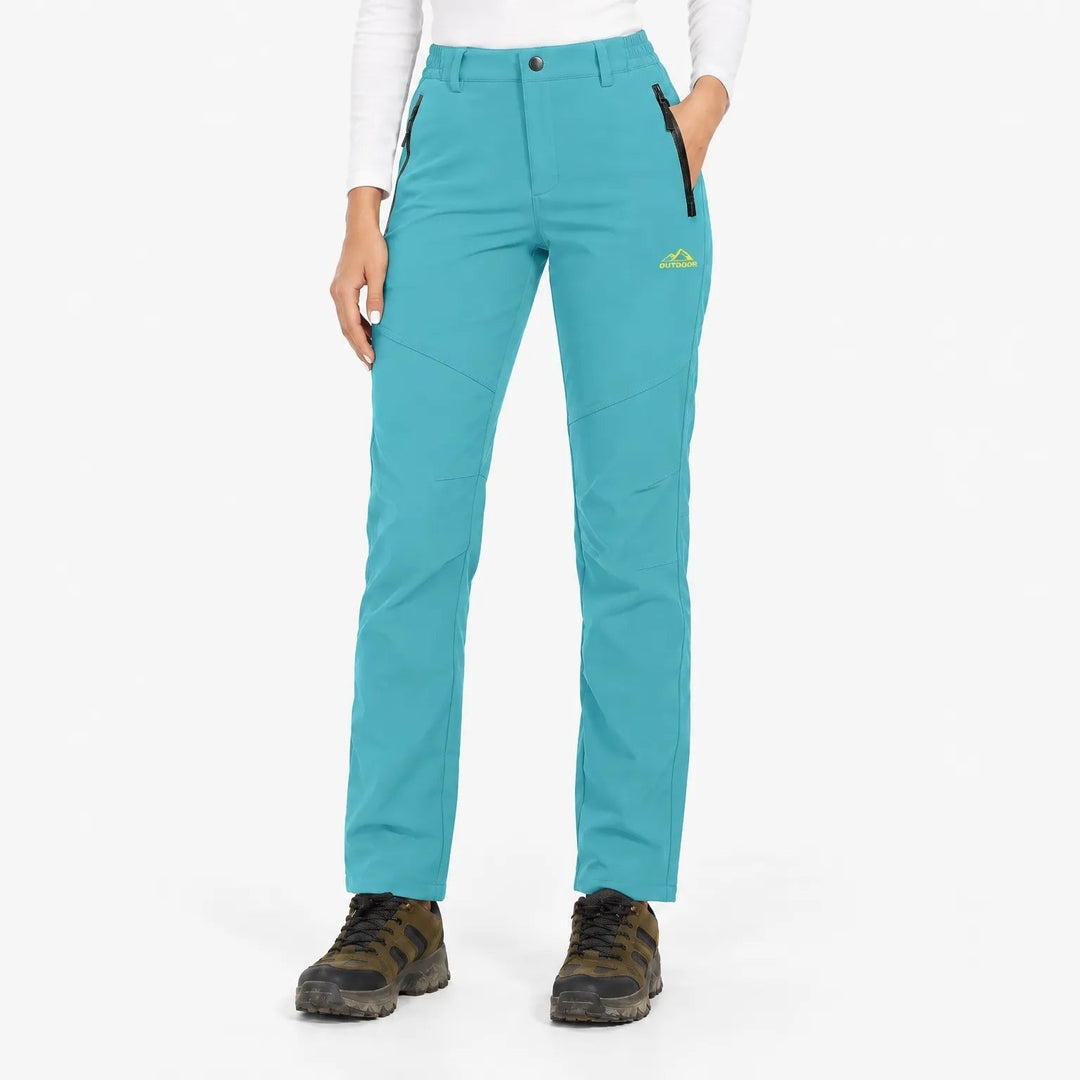 Vooraanzicht van de turquoise uitvoering van de broek, gedragen door een model met witte longsleeve en wandelschoenen 22