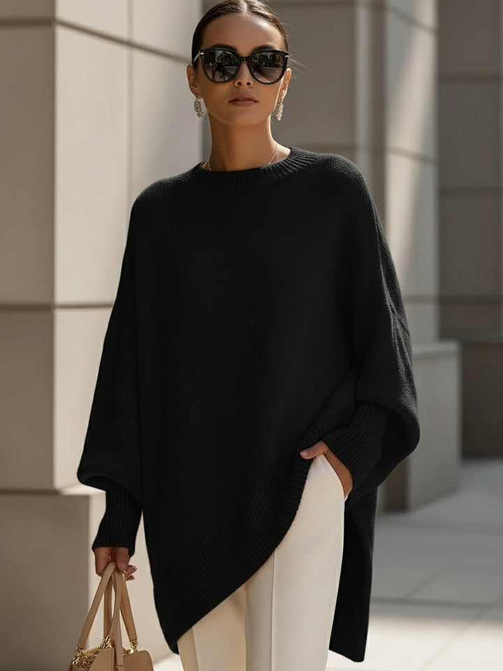 Model draagt de zwarte poncho met zonnebril, witte broek en beige handtas 7