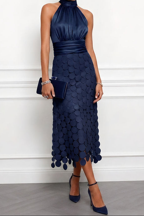 Model in de marineblauwe halterjurk met ronde applicaties op de rok, gecombineerd met donkerblauwe clutch en bijpassende pumps. 4