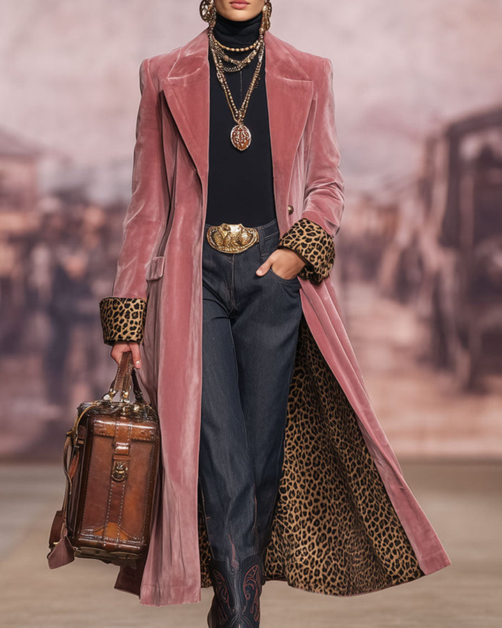 Model op een catwalk met vage stadsachtergrond draagt de roze fluwelen mantel met luipaardmanchetten, een hand in de zak en een leren tas. 3