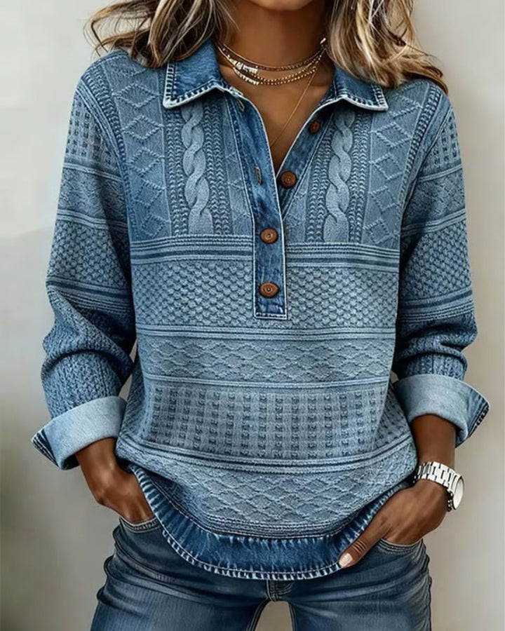 Model draagt de blauwe sweatshirt met kabelpatroon, houten knopen en omgeslagen mouwen, handen in de zakken van een spijkerbroek. 1