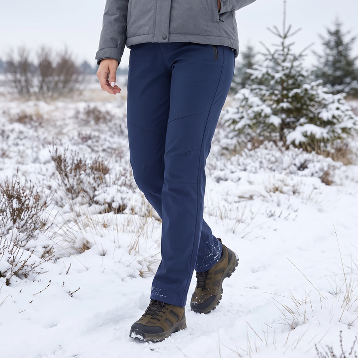 Vrouw in marineblauwe broek en wandelschoenen loopt door een besneeuwd heidelandschap met sparren 1
