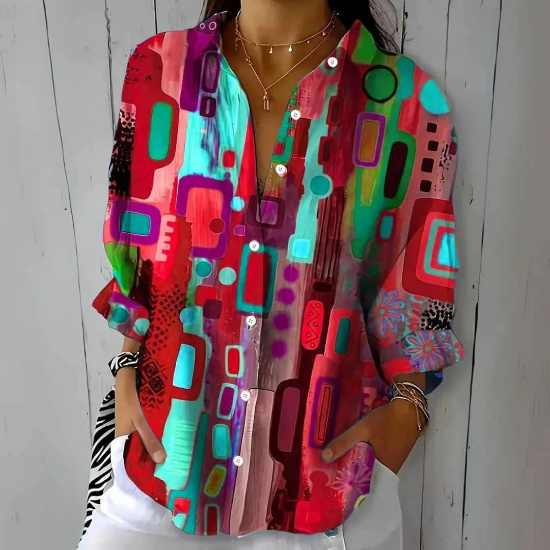 Dezelfde blouse in rode en turquoise tinten met paarse vormen, gedragen door een model met gouden kettingen en armbanden. 4