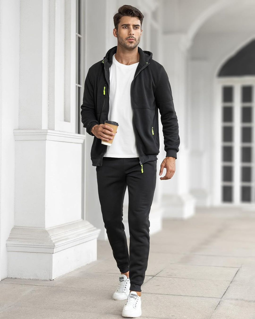 Model wandelt met koffie in zwart trainingspak met open vest en wit shirt 24