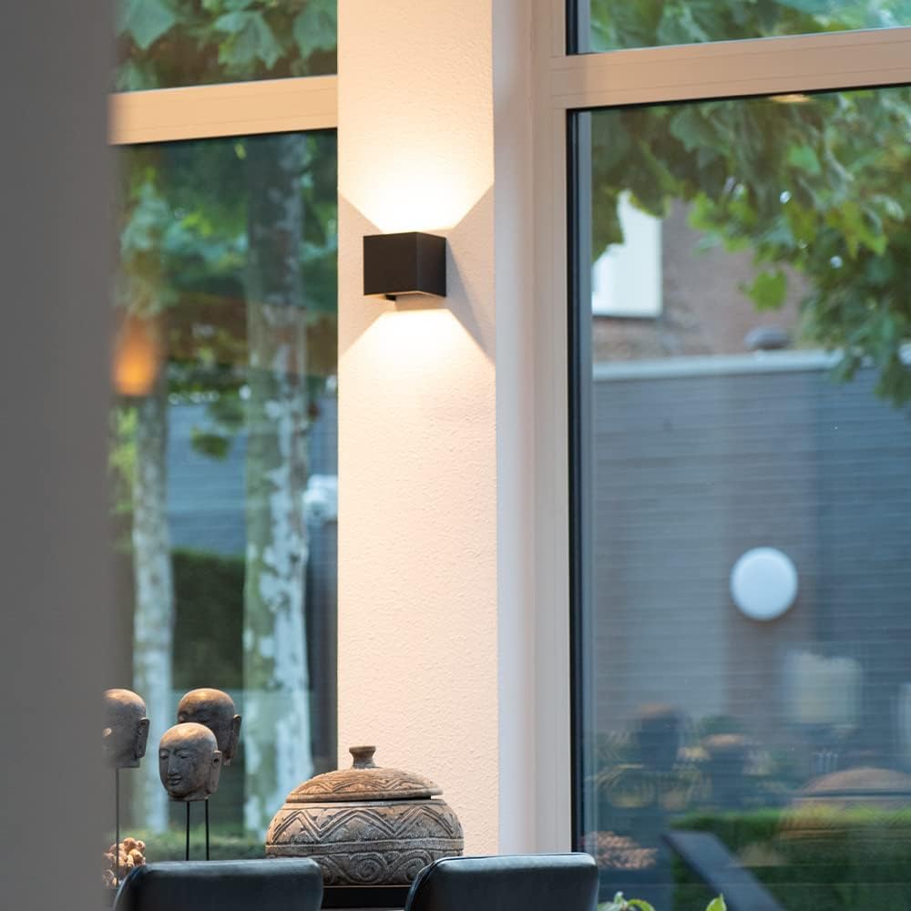 Zwarte kubuslamp op een witte pilaar tussen grote ramen, met verlicht uitzicht op een tuin. 8