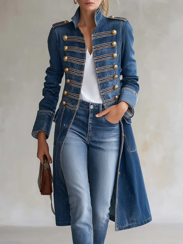 Model in blauwe denim jas met gouden knopen en galon, gedragen met wit topje, jeans en bruin handtasje, handen losjes in zak. 1