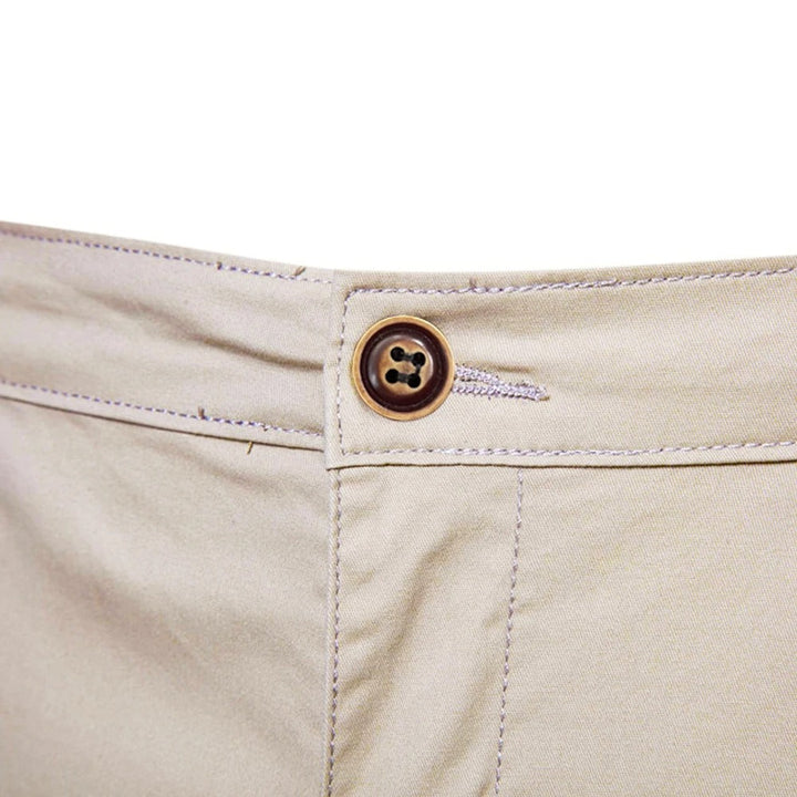 Close-up van de bruine knoop en het knoopsgat aan de tailleband van de beige short. 5