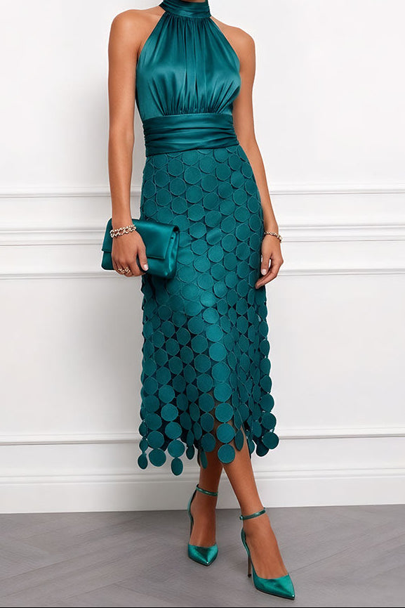 Model draagt de halterjurk in diep groenblauw met applicaties op de rok, met bijpassende satijnen clutch en pumps. 6