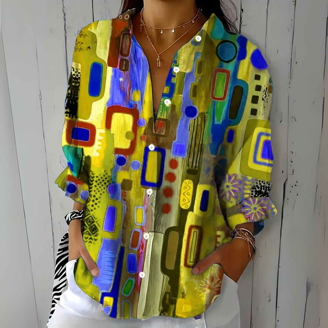 Blouse in gele en blauwe tinten met abstract patroon, losvallend gedragen met witte broek en een zebraprint haarband om de pols. 5
