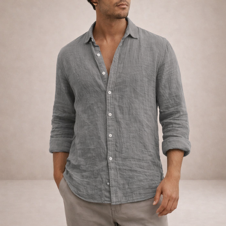 Model in grijs linnen overhemd met opgerolde mouwen en een hand in de zak van een beige broek, bijgesneden vanaf de kin. 2