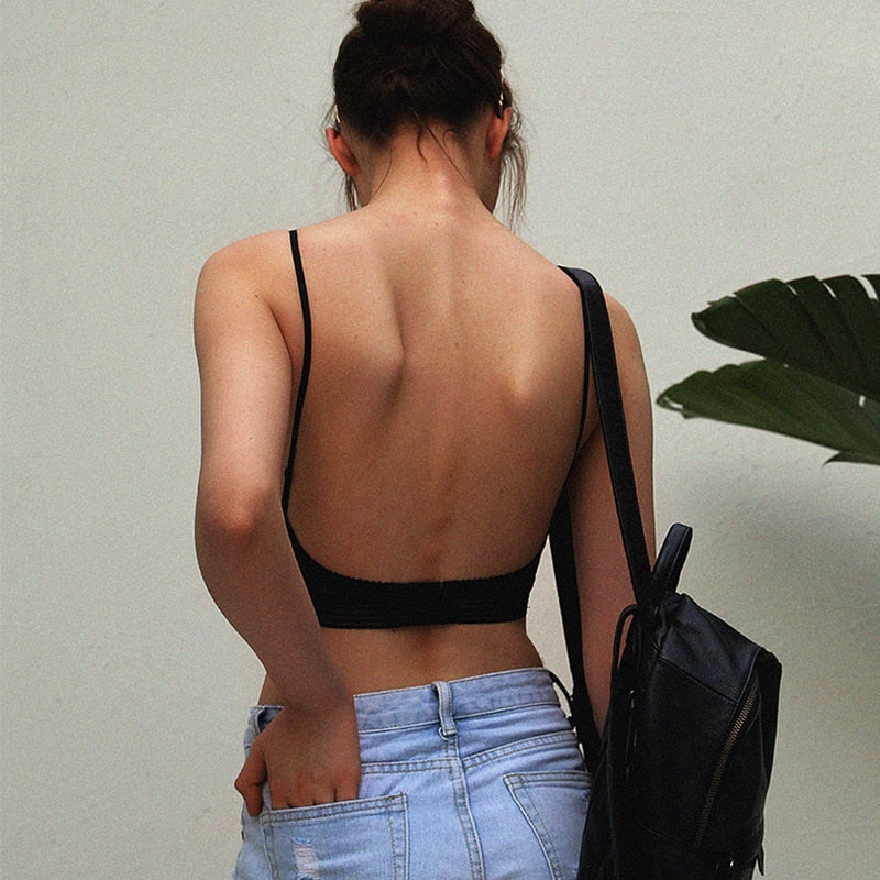 Rugzijde van een model in de zwarte bralette met open rug en dunne bandjes, met rugzak en spijkerbroek. 2