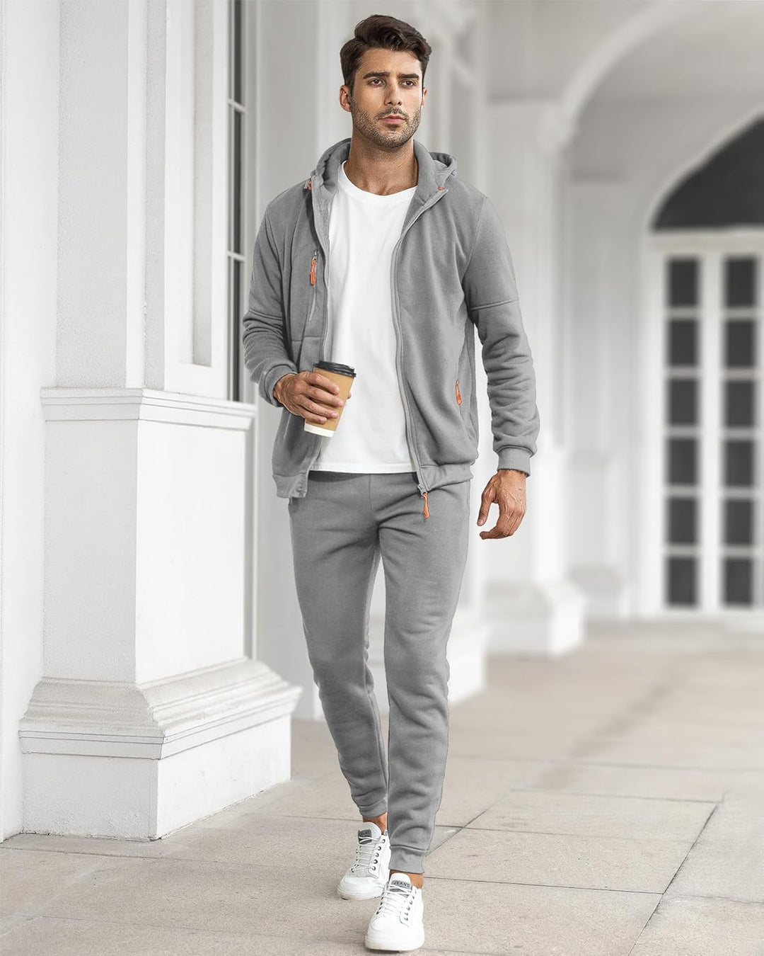 Man loopt buiten in grijs trainingspak met open vest, wit shirt en koffie in de hand 31