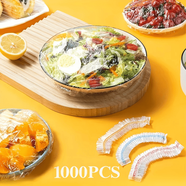 Afgedekte salade, fruitschaal en tomaten op een gele ondergrond, met drie losse kappen met gekleurde elastiekrand rechtsonder. 9