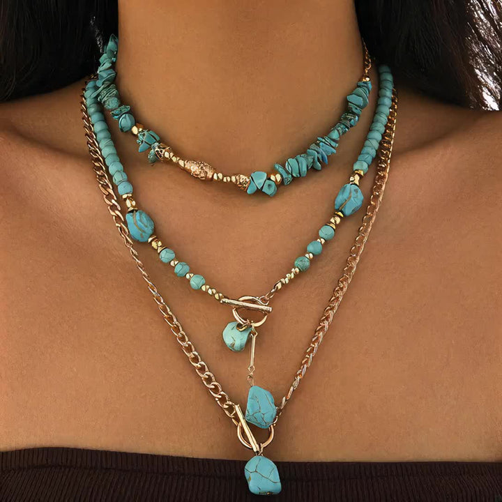 Dichtbij beeld van de drie gelaagde turquoise kettingen met gouden details, gedragen door een model 8