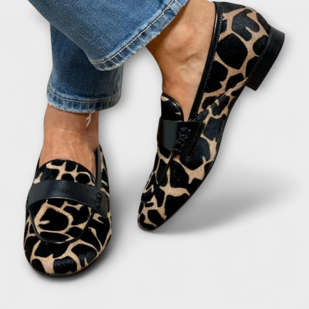 Voorkant en zijkant van beide gedragen loafers, met zwarte leren band over de wreef, lage zwarte hak en gestikte rand, naast een jeans. 3