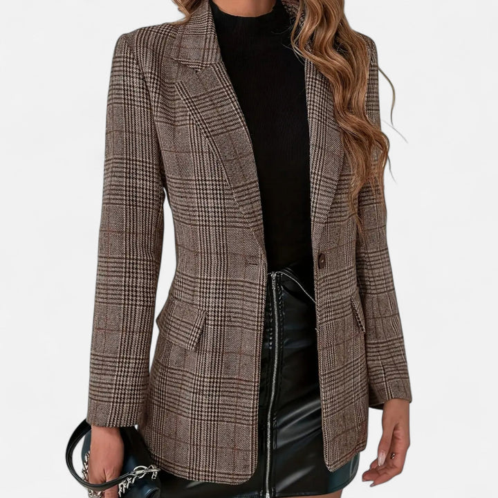Model draagt de bruin geruite blazer open over een zwarte coltop en een zwart rokje, voorkant met revers, klepzakken en een knoop. 1
