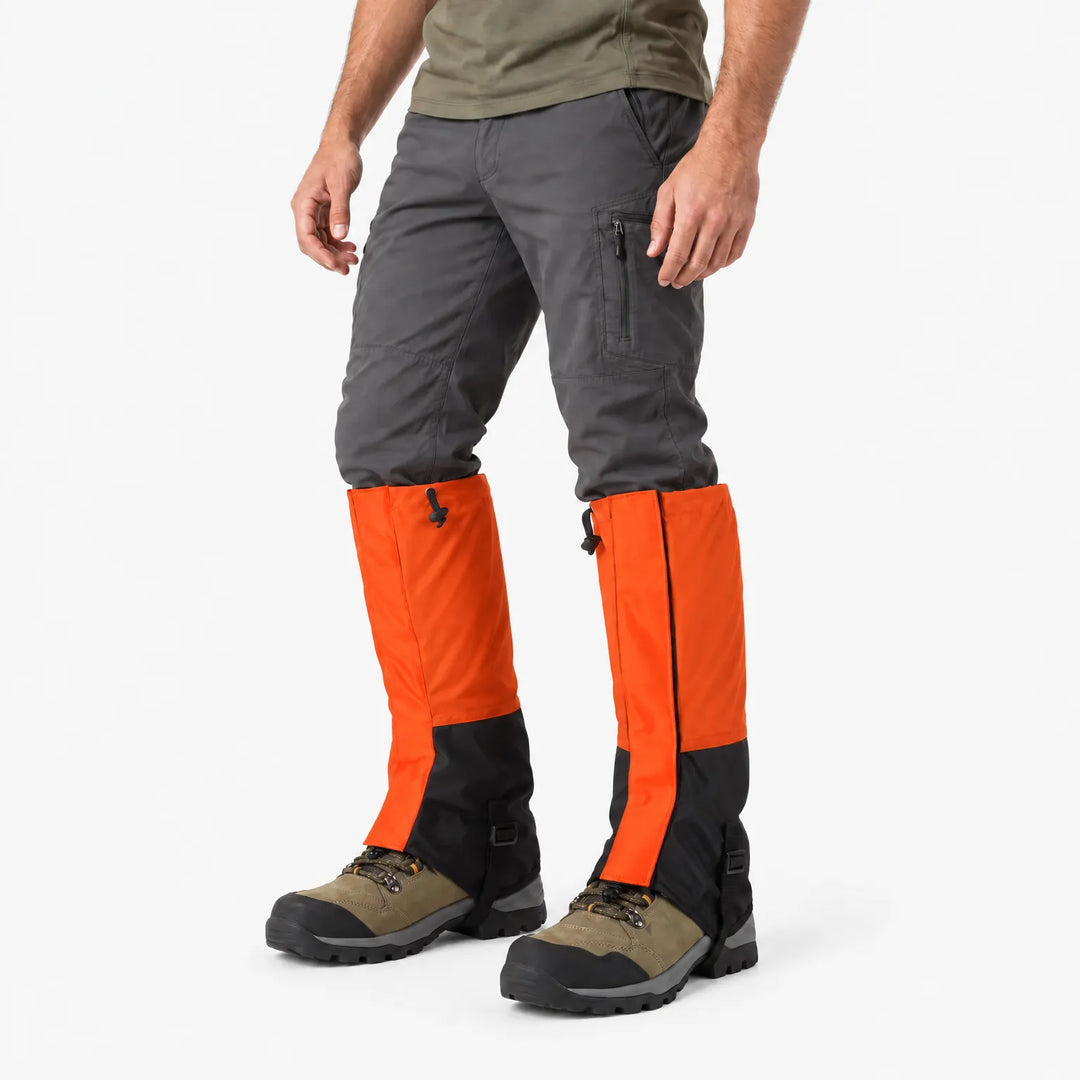 Oranje gamaschen met zwart onderstuk, schuin van opzij gedragen over wandelschoenen en een grijze broek, tegen een witte achtergrond. 4